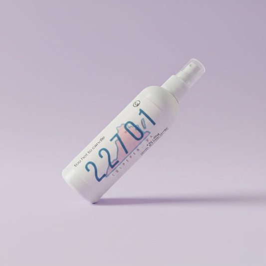 A white spray bottle labeled '22701' with blue and pink graphic details, photographed diagonally on a solid light purple background.
